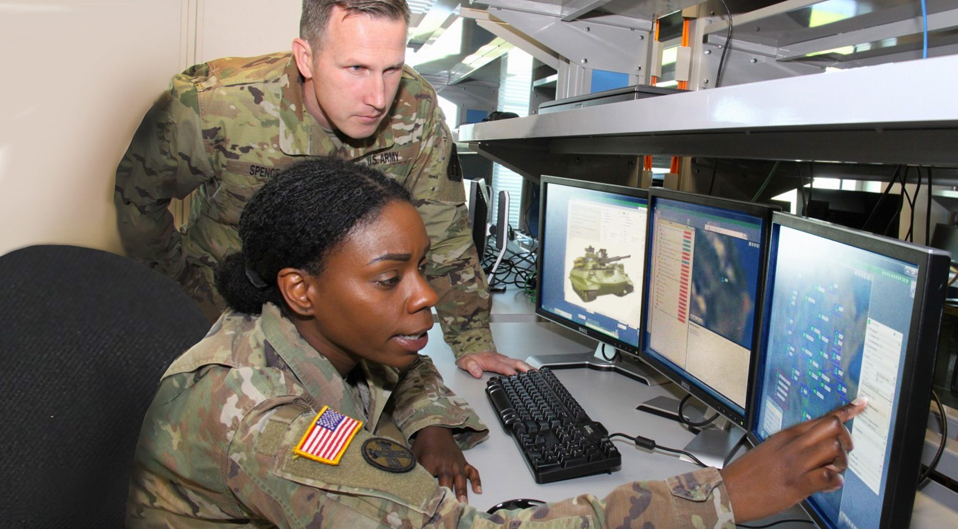 Two US Army soldiers looking at computer monitors showing images of robotic combat vehicles.