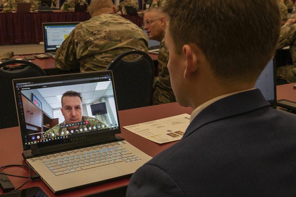 Man watching soldier speaking on laptop. Other soldiers in background on laptops.